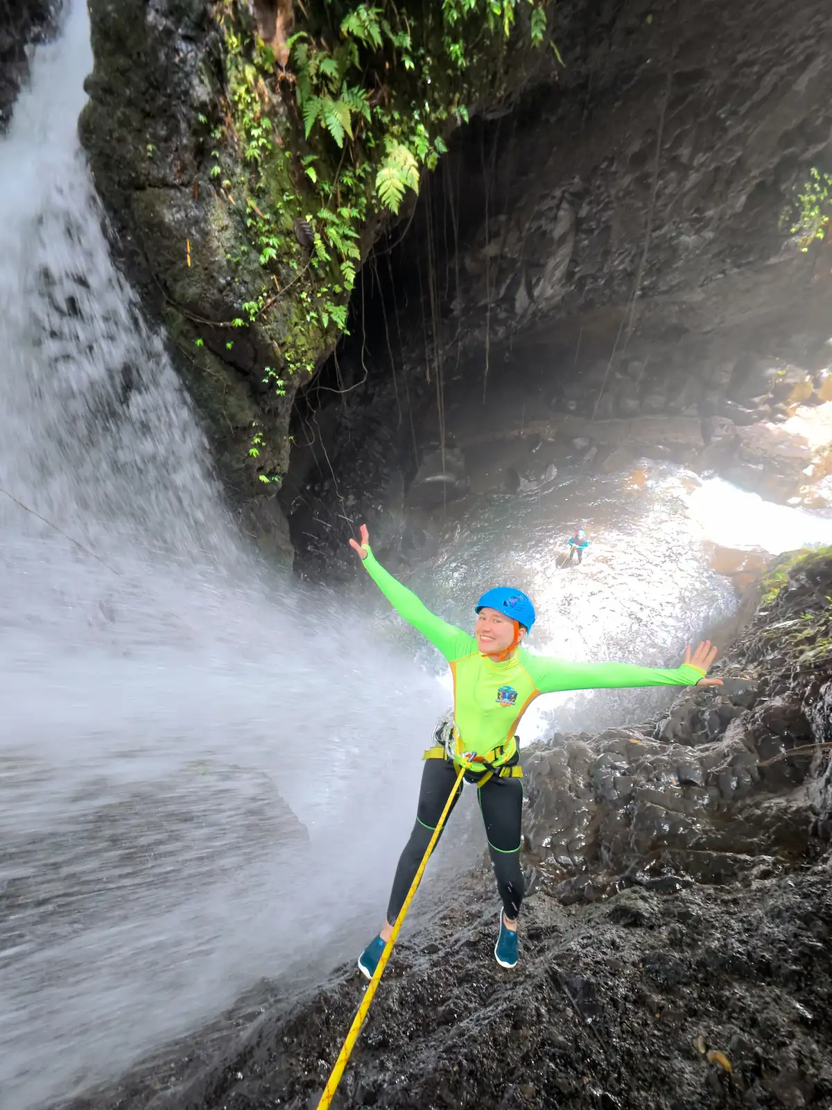 Smiling guest rappelling beside a jungle waterfall