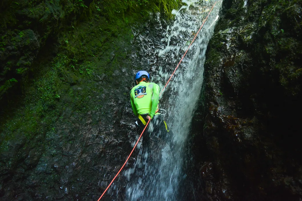 Three canyoners descending on blue and orange ropes with guide-managed rope systems in a mossy North Bali canyon