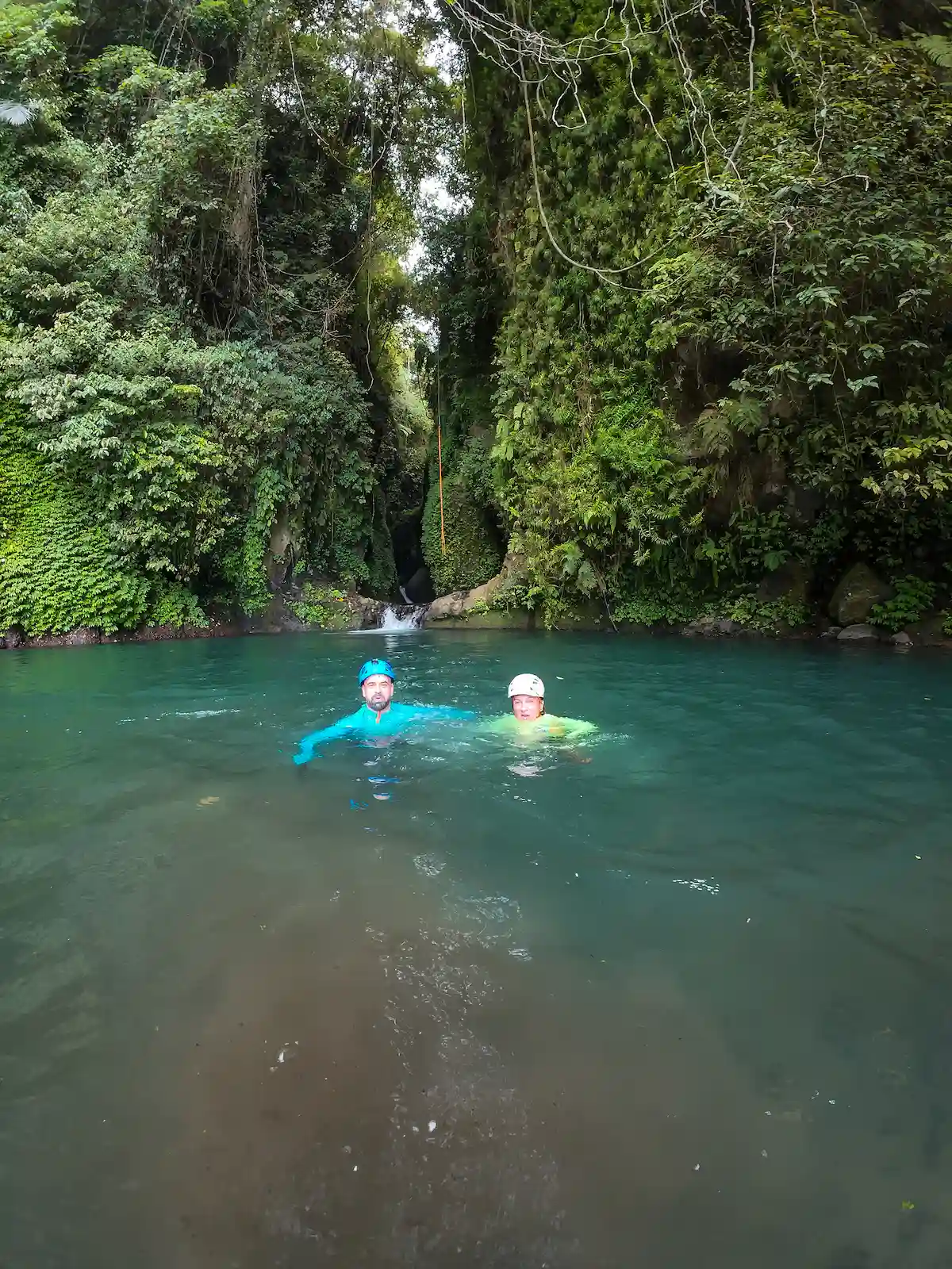 Two guests swimming through a turquoise natural pool with a guide