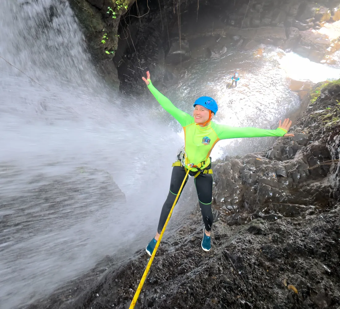 A canyoner rappelling on rope beside a waterfall under guide supervision in North Bali
